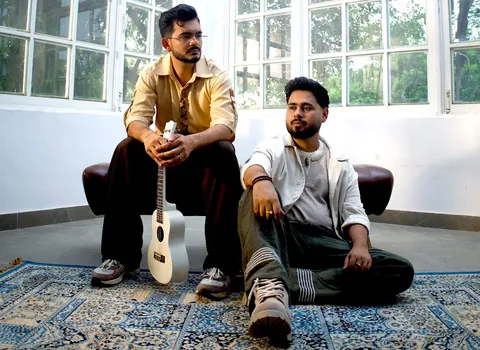 Banjaare, the Haryanvi duo, in a sunlit room, one seated with a white ukulele and the other sitting on a rug
