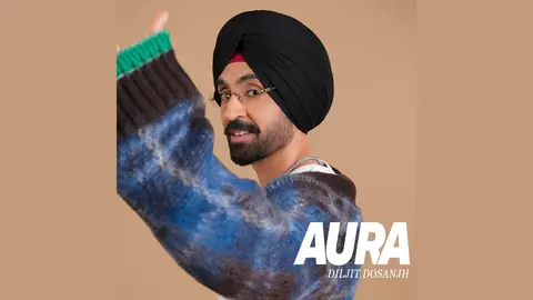 Diljit Dosanjh in a black turban, glasses and a blue knit sweater, waving on the Aura album art