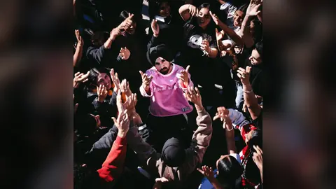 Diljit Dosanjh in a pink sweatshirt and black turban surrounded by raised hands, on the official cover of his EP The Call of Panjab