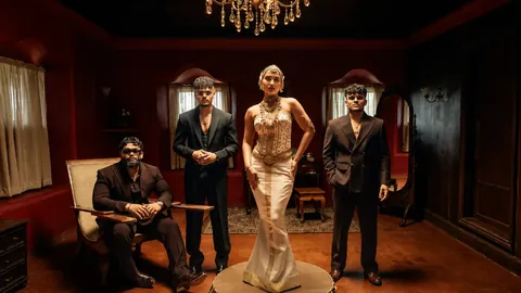 Shreya Ghoshal in a white gown on a round plinth with the Kalyani Remix artists in a red wood-panelled room
