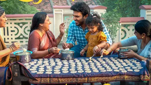 Kiran Abbavaram laughs at a long table with family members pouring batter into rows of small moulds, in official artwork for the Reality single